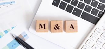 Wooden blocks with the characters 'M&A' spelled out on top of an open laptop